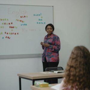 A teacher explaining English concepts to a student in a classroom setting with a whiteboard.